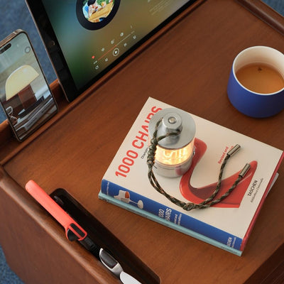Desk setup with tablet, smartphone, book titled '1000 Chains', and a small lamp.