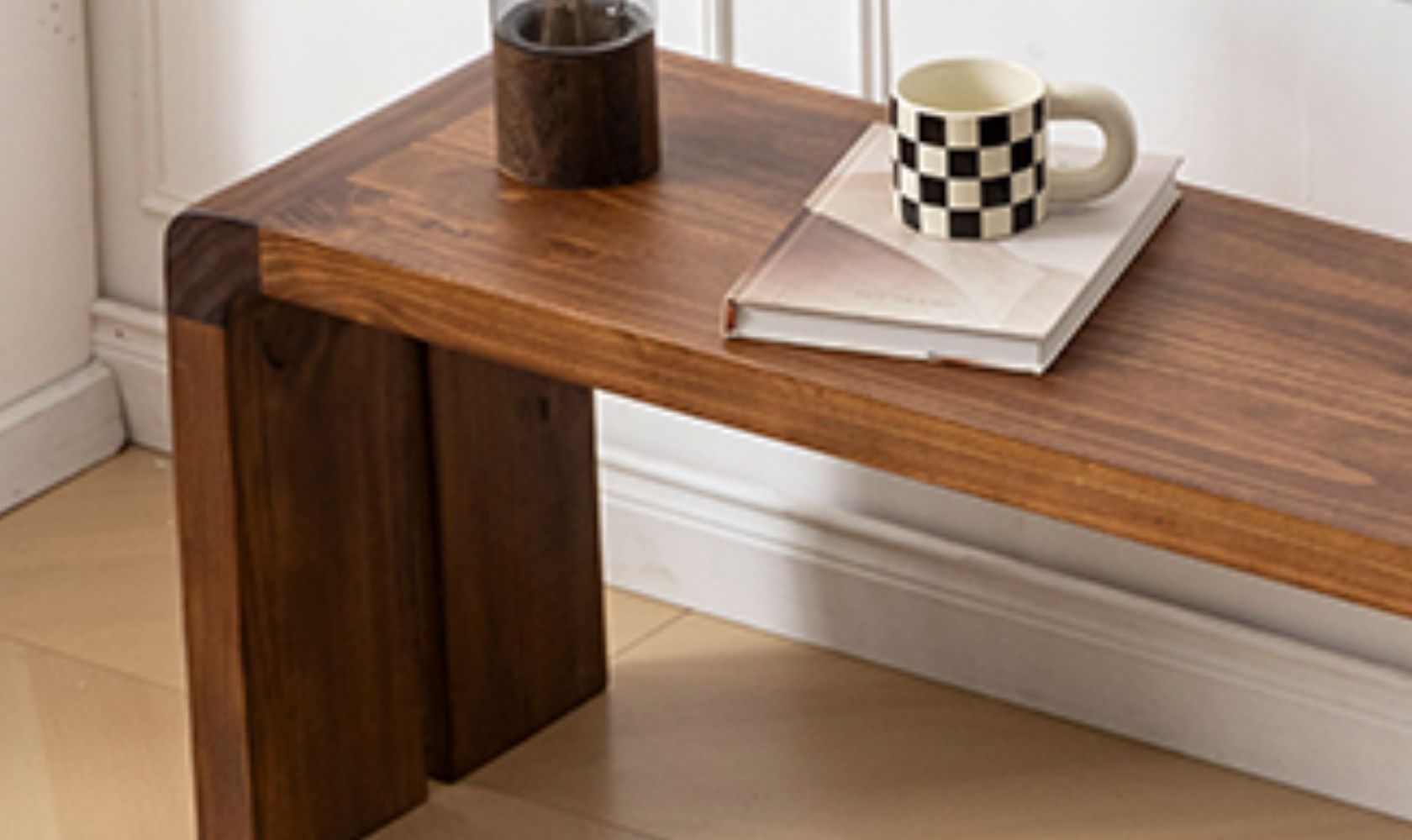Wooden desk with a checkered mug, black mug, and book on top in a room.