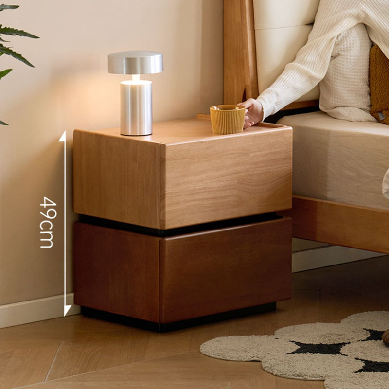 Wooden nightstand with a lamp and cup next to a bed in a bedroom setting.