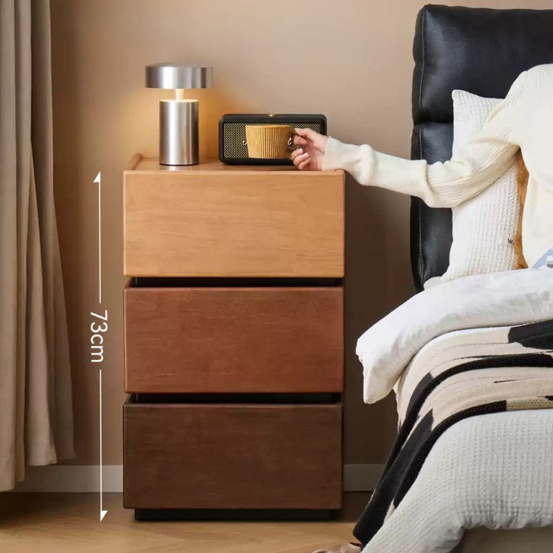 Wooden nightstand with two drawers next to a bed, showing a hand reaching for a small device.