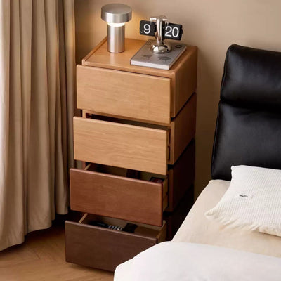 Wooden nightstand with drawers next to a bed in a bedroom setting.